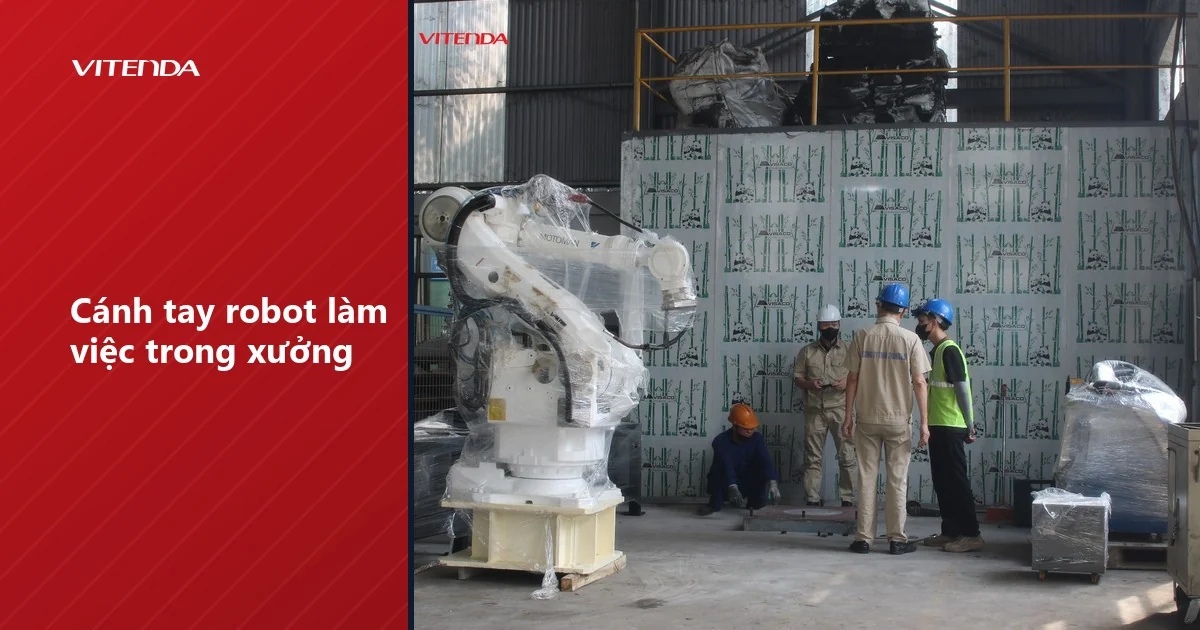 Cánh tay robot công nghiệp đóng màng bọc đặt trên bệ trong nhà xưởng, kỹ thuật viên đứng cạnh