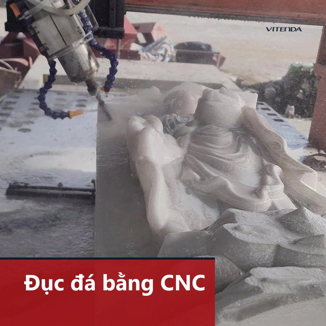Đầu dao máy CNC đang đục phôi đá thành tấm phù điêu, nước làm mát chảy trên bề mặt