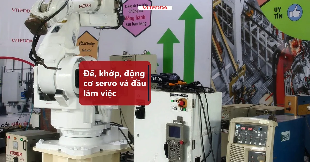 Cánh tay robot công nghiệp màu trắng cạnh tủ điều khiển và màn hình dạy, thấy đế, các khớp và đầu làm việc