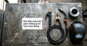 Bộ phụ kiện máy hàn gồm kìm hàn, kìm kẹp mát, mỏ MIG, cuộn dây hàn và mặt nạ bày trên bàn thợ